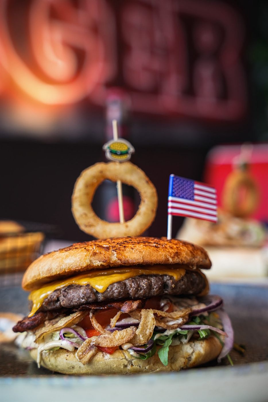 Bacon Cheeseburger mit Onion Ring und US-Flagge vor dem Jack's-Neonschild
