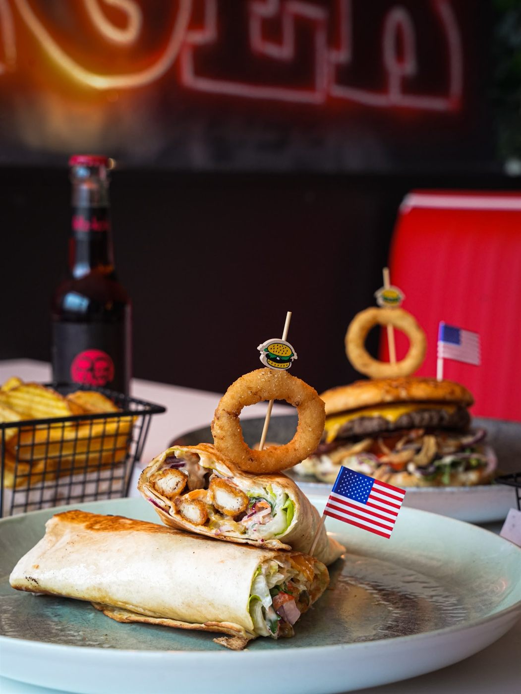 Aufgeschnittener Crispy Chicken Wrap mit Onion Ring am Spieß vor roter Neon-Kulisse