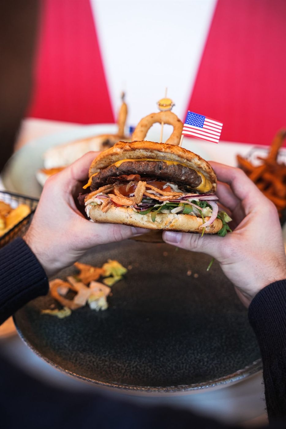 Saftiger Burger wird mit beiden Händen über einem dunklen Teller gehalten