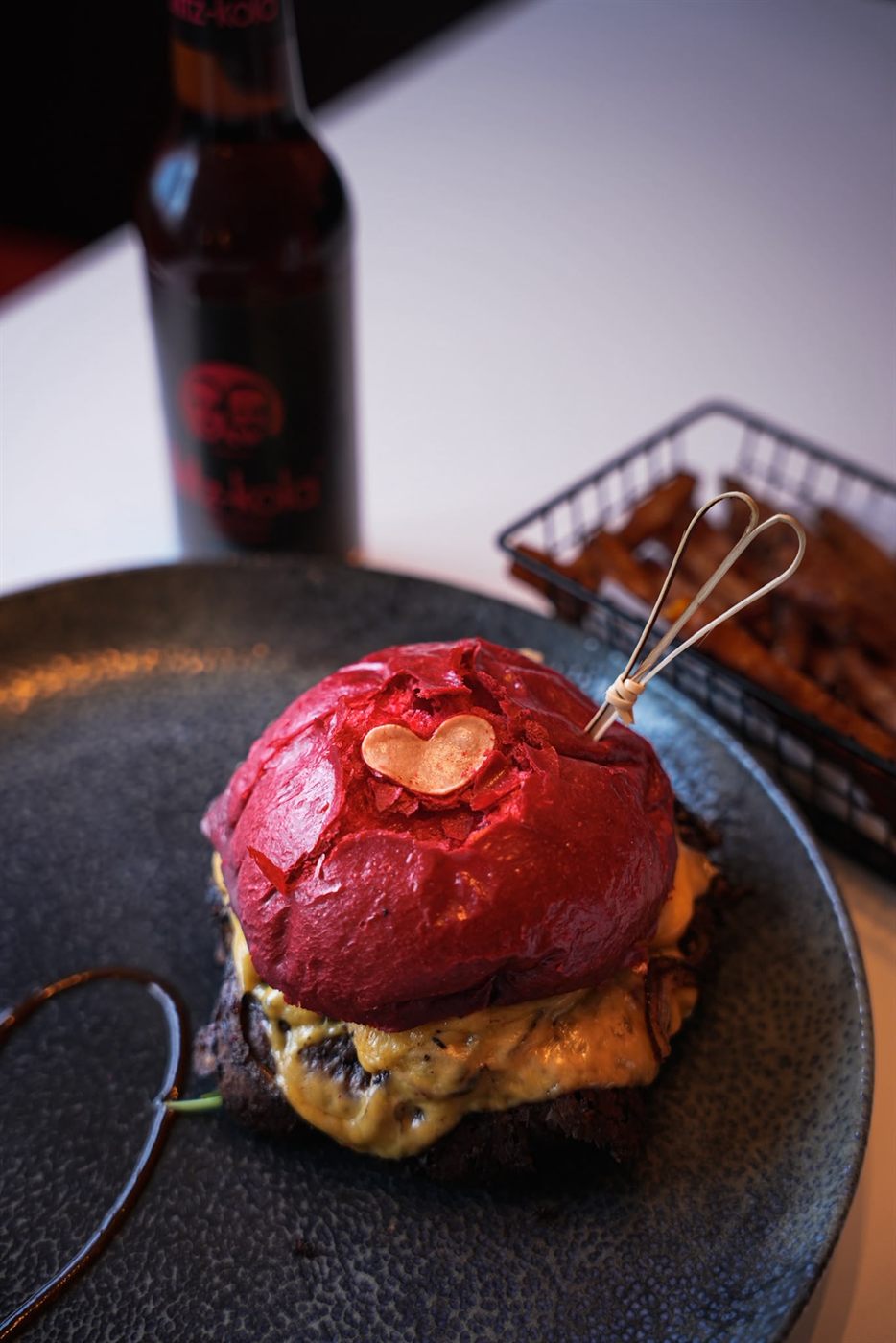 Burger mit leuchtend rotem Beetroot-Bun und Herz-Deko auf dunklem Teller